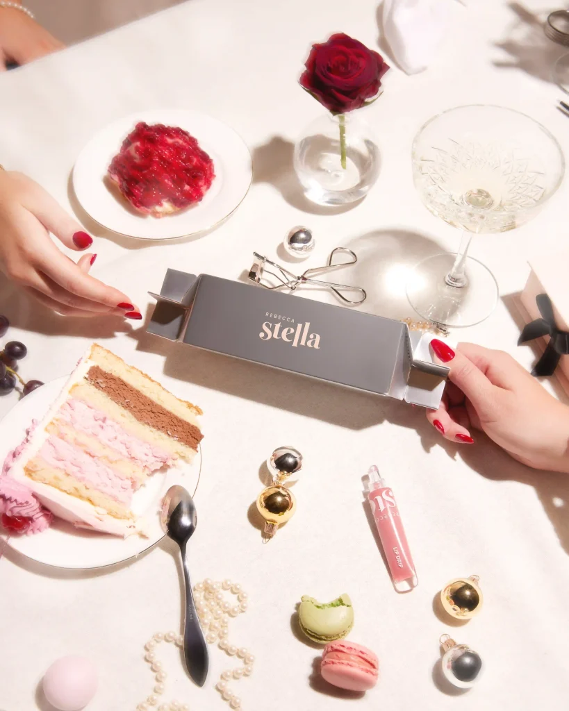 Lyxig julbox från Rebecca Stella Beauty ("The Gift Box") fotograferad i studio. Boxen är öppen och visar ett innehåll av läppstift, lip liner och kosmetik mot en sofistikerad beige bakgrund. Skapat av produktfotograf i Stockholm för skönhetskampanjer.