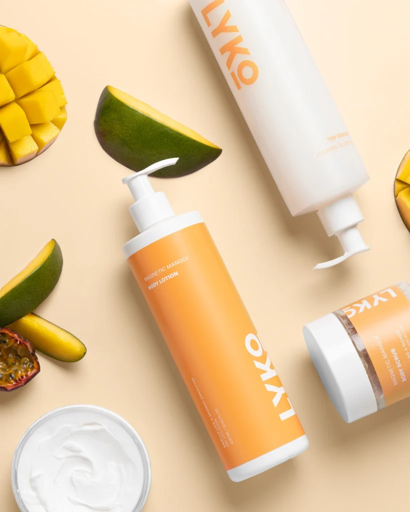 Professionell produktfotografering av By Lyko Magnetic Mango-serien. Bilden är tagen uppifrån (flatlay) i en studio och visar body lotion, shower gel och scrub omgivna av färsk mango och passionsfrukt. Skapad av en content producer i Stockholm med fokus på skönhetsprodukter och lifestyle-estetik.