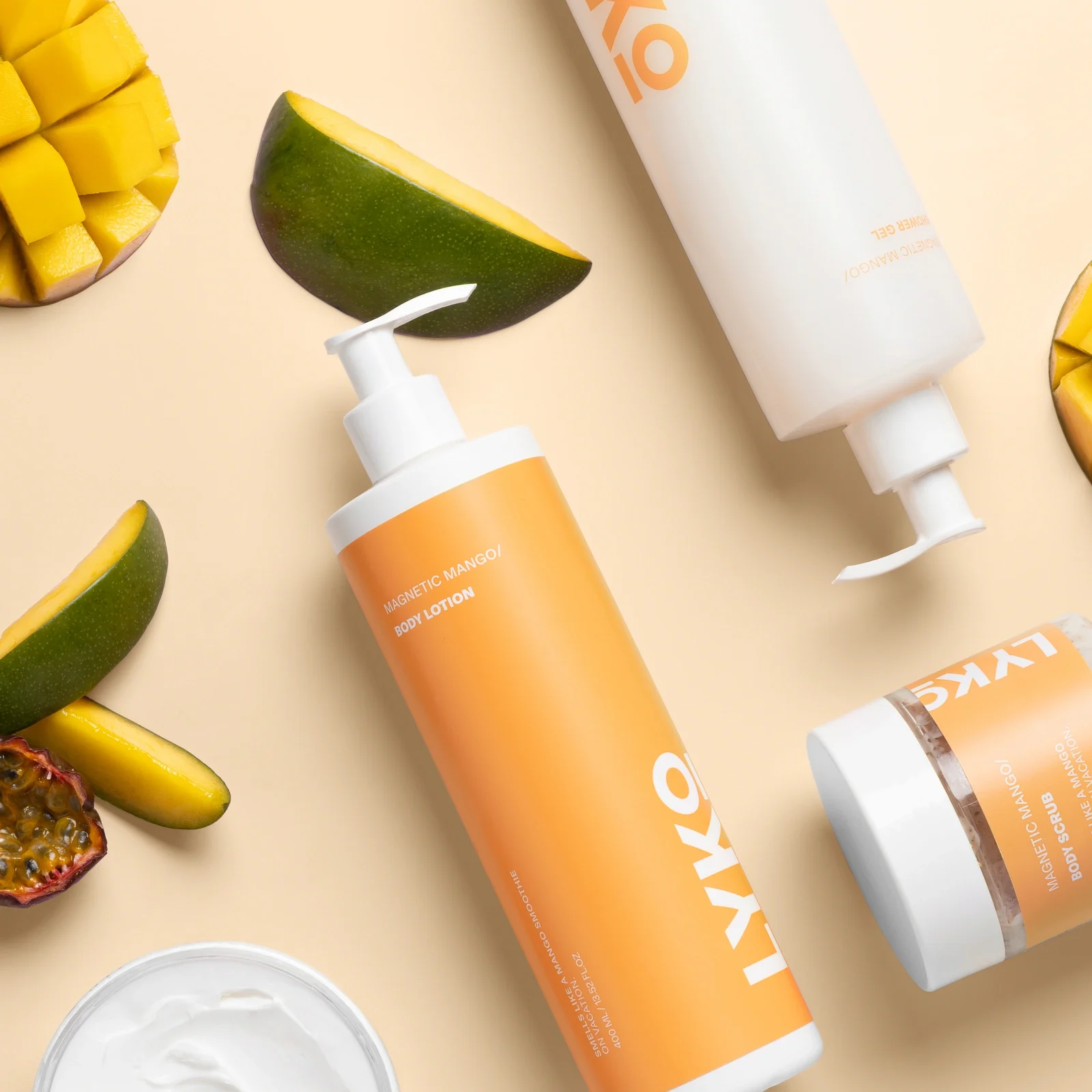 Professionell produktfotografering av By Lyko Magnetic Mango-serien. Bilden är tagen uppifrån (flatlay) i en studio och visar body lotion, shower gel och scrub omgivna av färsk mango och passionsfrukt. Skapad av en content producer i Stockholm med fokus på skönhetsprodukter och lifestyle-estetik.