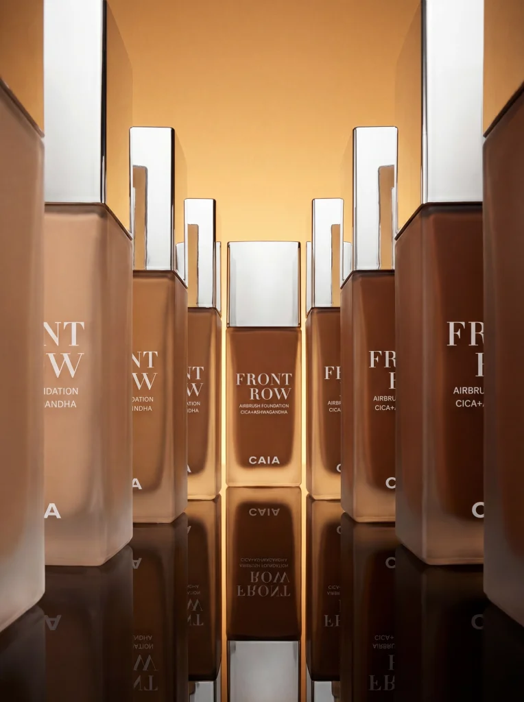 Lyxig produktuppställning av CAIA Cosmetics Front Row Foundation i olika nyanser med speglingar, AI-genererad bild från Sköneskog Studio.